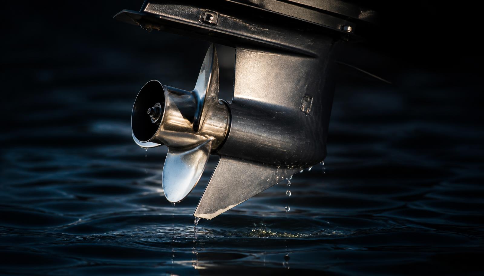 Outboard lower unit and stainless propeller lifted above dark water