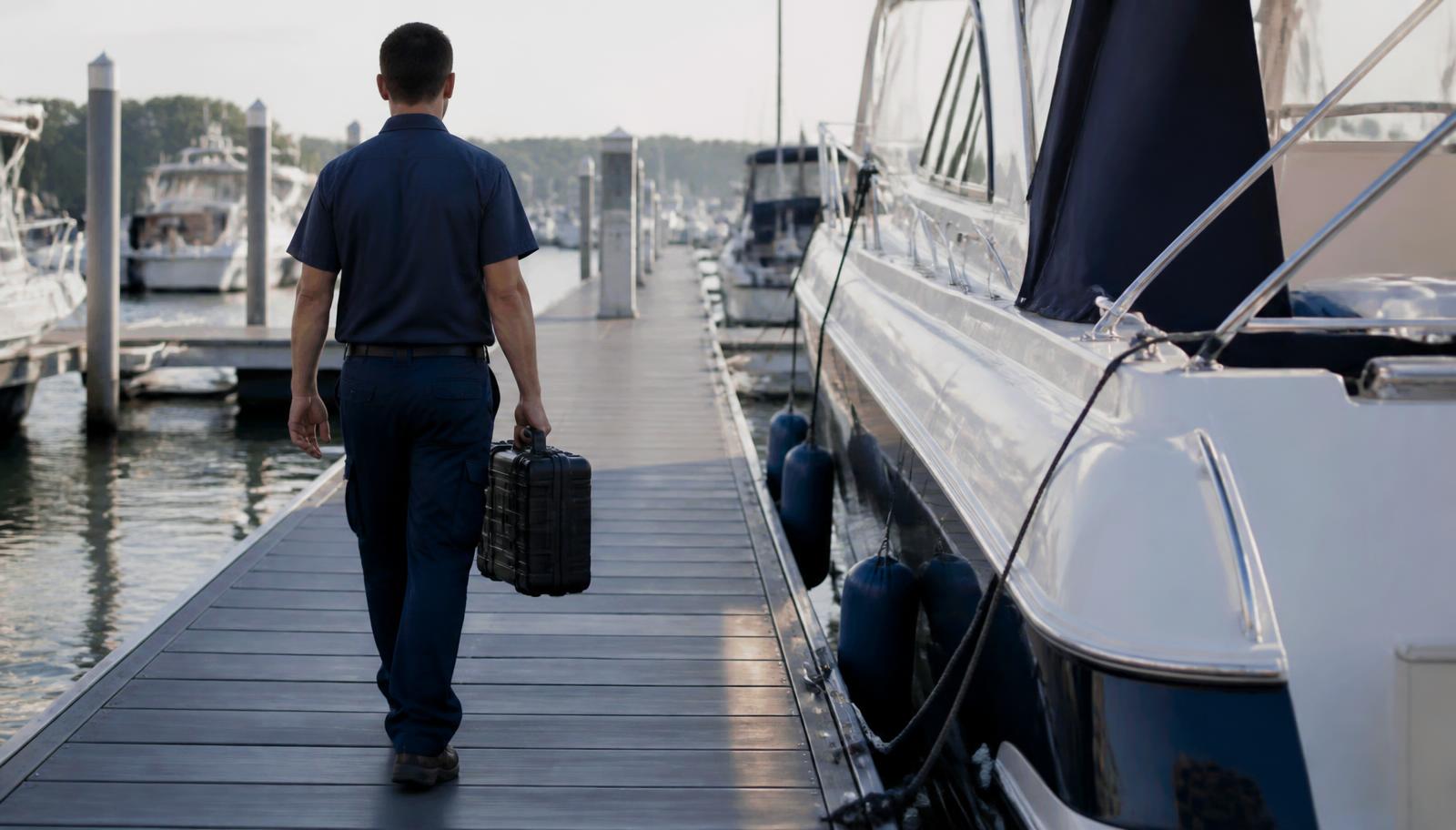 Marine technician walking down a marina dock carrying a tool case